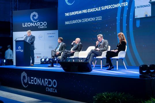 on stage, anders dam jensen at the podium, and the four other panellists sitting on chairs to the right