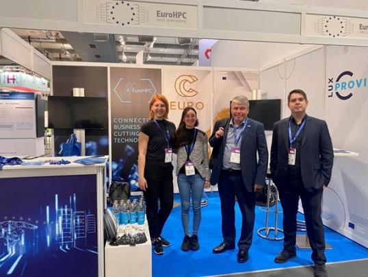 2 women and two men standing in a exhibition booth, in the background we can see the FF4EuroHPC, EuroCC and LuxProvide logos.